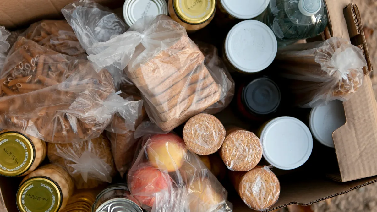 A collection bin overflowing with canned goods outside a shop.