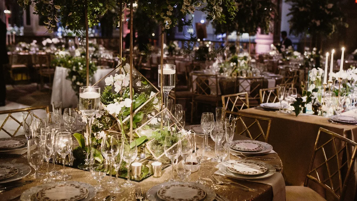 Elegant round dinner tables with candles and centerpieces of vegetables and flowers.