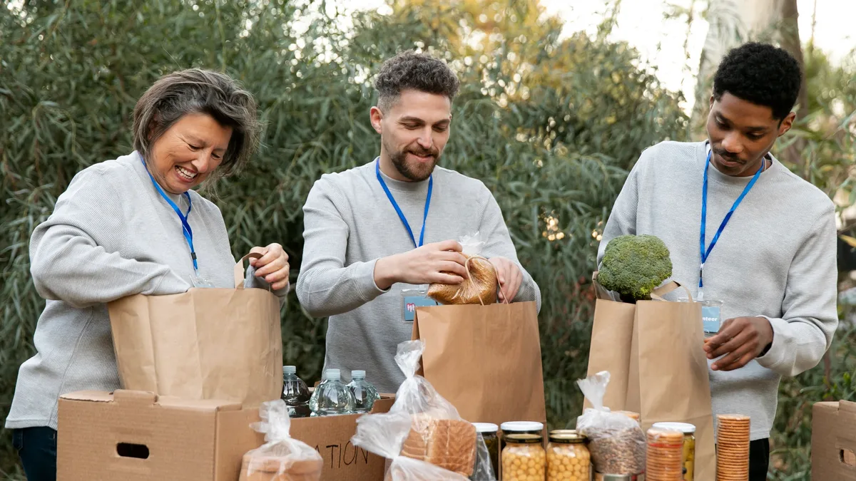 Volunteers filling backpacks at a long table, hands only.